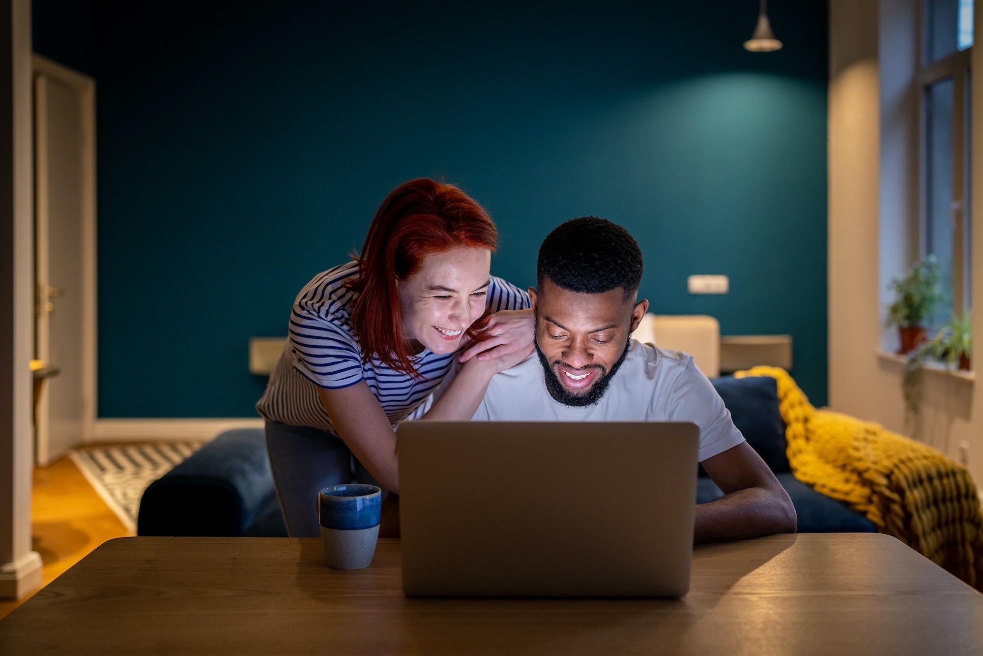 Happy smiling interracial couple man and woman look at laptop screen choosing movie in evening