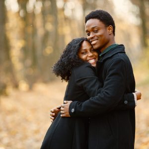 Black young man and his girlfriend hugging. Romantic couple walking in autumn park. Man and woman wearing black coats.